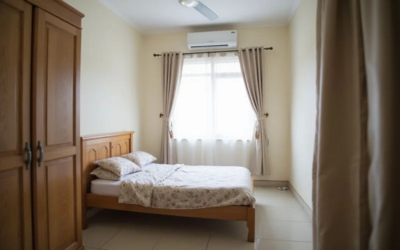 A simply furnished budget homestay bedroom in Malaysia with a bed, small table and window with natural daylight